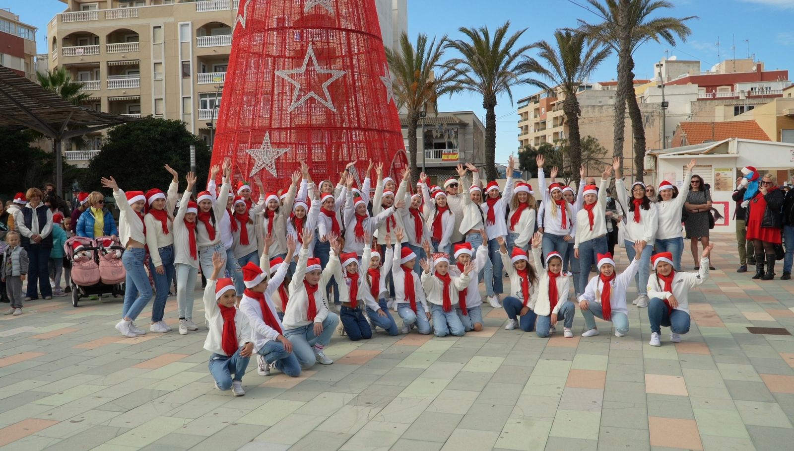 Grupo de baile con gorros de Papá Noel junto al árbol rojo